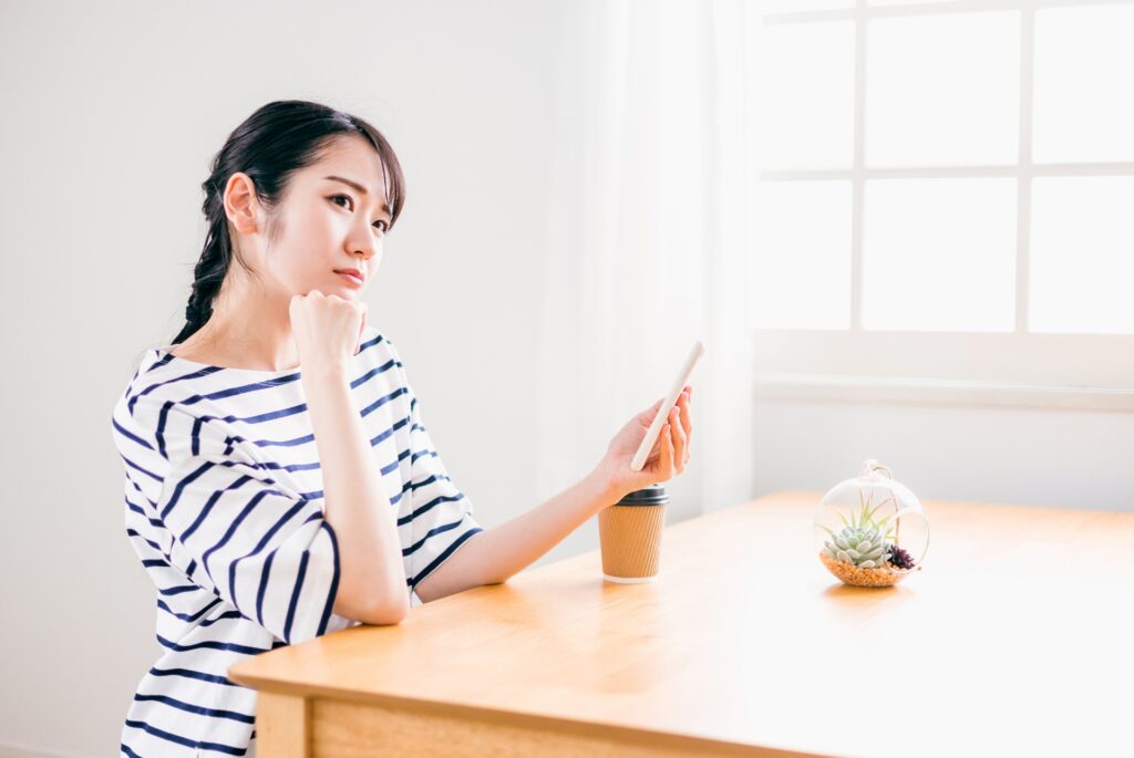 スマートフォンを持って考え込む女性